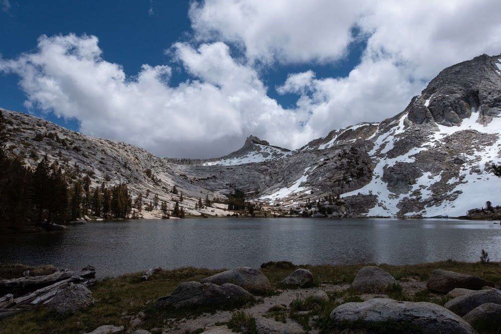 Lake surrounded by tall grey mountains with snow, and a particularly pointy one right behind the lake